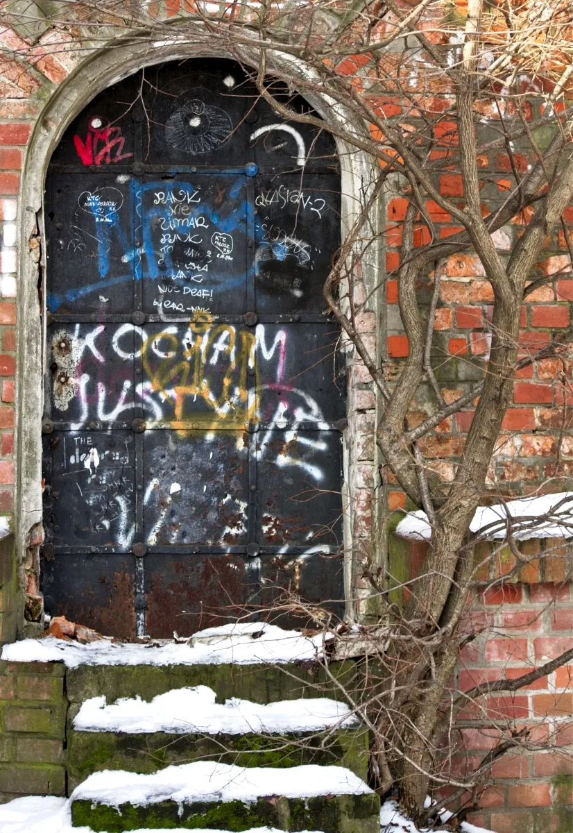 Graffiti-covered black door set in a red brick archway
